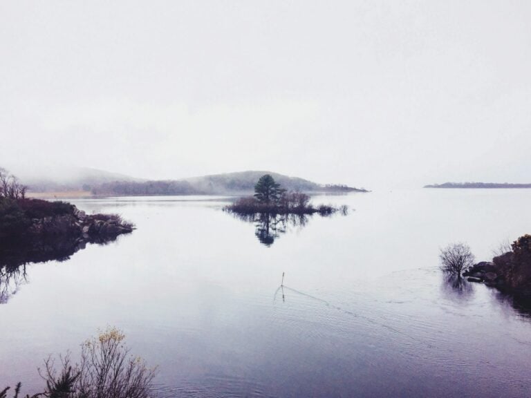 Serene lake in County Mayo dotted with small tree-covered islands, rolling hills in the distance, mist rising from the lake